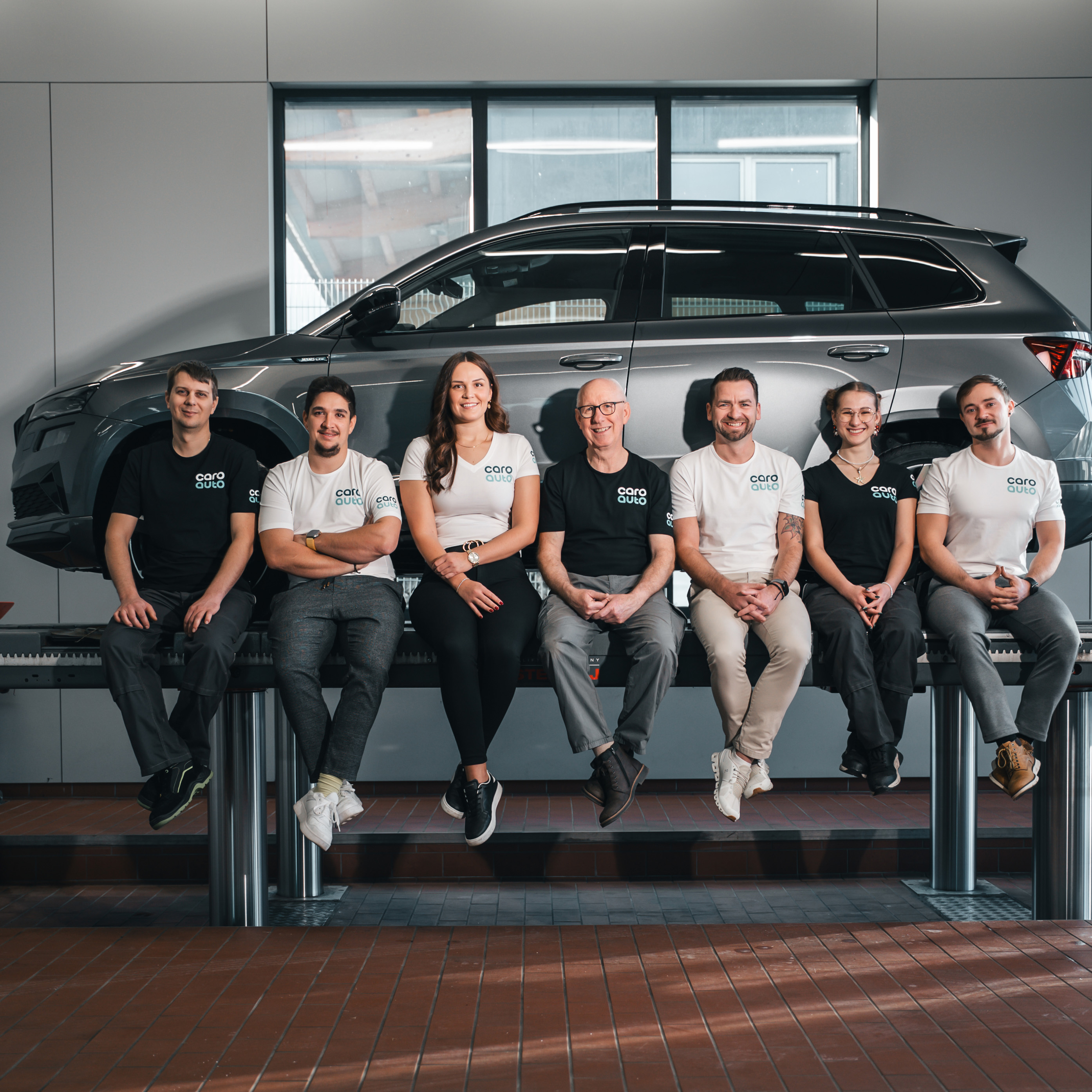 Das Caro Team sitzt auf einer Hebebühne vor einem Auto.
