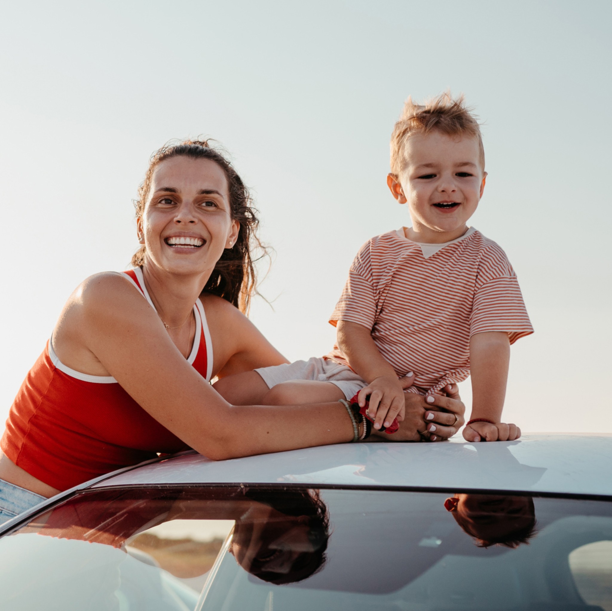 Mutter und Sohn sitzen auf dem Dach eines Autos am Strand