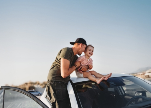 Junger Vater und sein Sohn sitzen auf dem Dach seines Autos