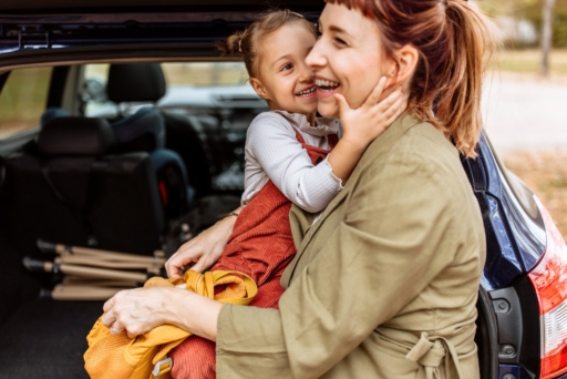 Ein Foto zeigt eine Mutter und ihre Tochter, die im Auto Rucksäcke packen und dabei ihre Verbundenheit und Liebe zueinander spüren. Sie bereiten sich auf ein Wanderabenteuer vor.